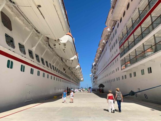 A tourist is dwarfed by the two large docked ships in the pier